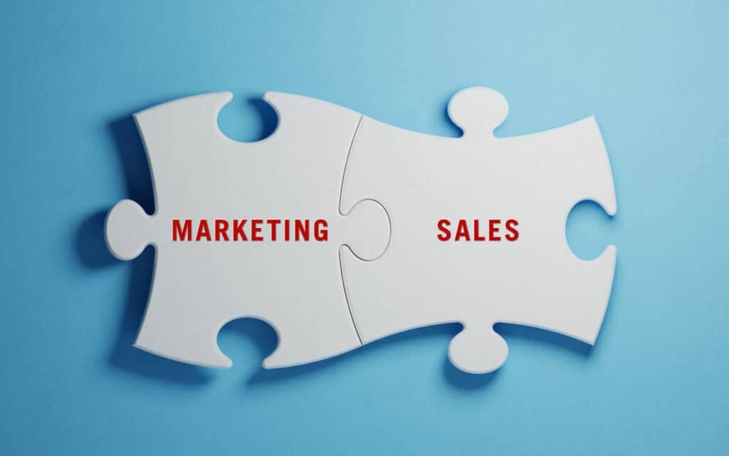 White jigsaw puzzles on blue background. Marketing and Sales writes on jigsaw puzzle pieces. Horizontal composition with copy space. Great use for marketing concepts.
